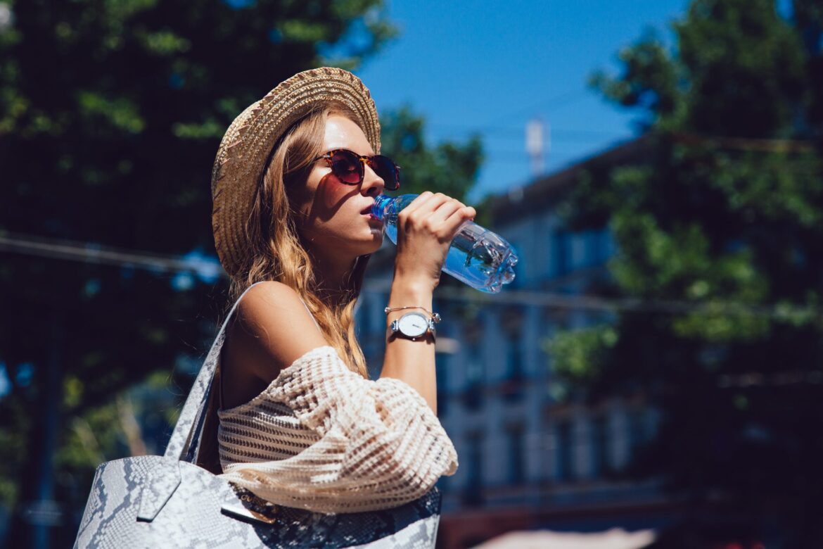 beautiful-young-woman-sunglasses-drinking-water-from-bottle-walking-outdoors-min